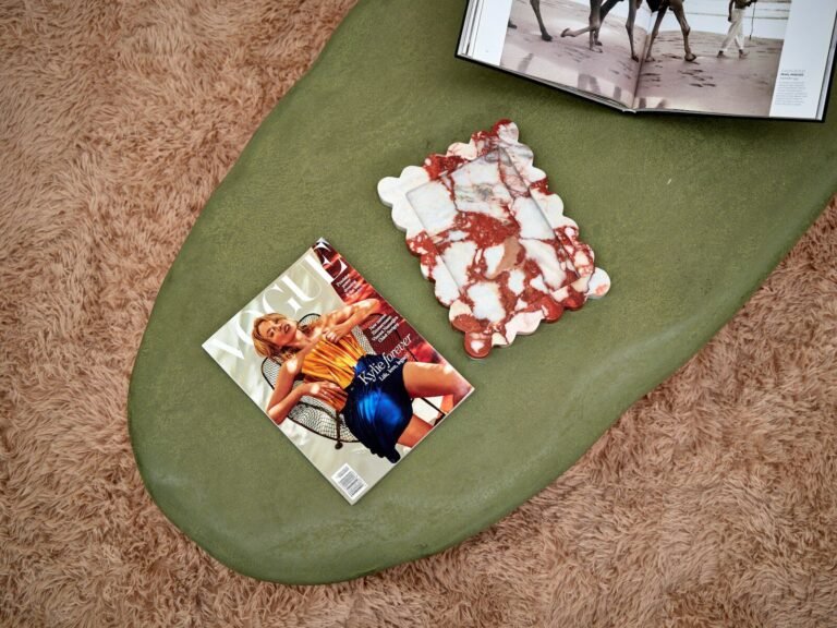 A magazine and a scalloped marble tray on a green coffee table