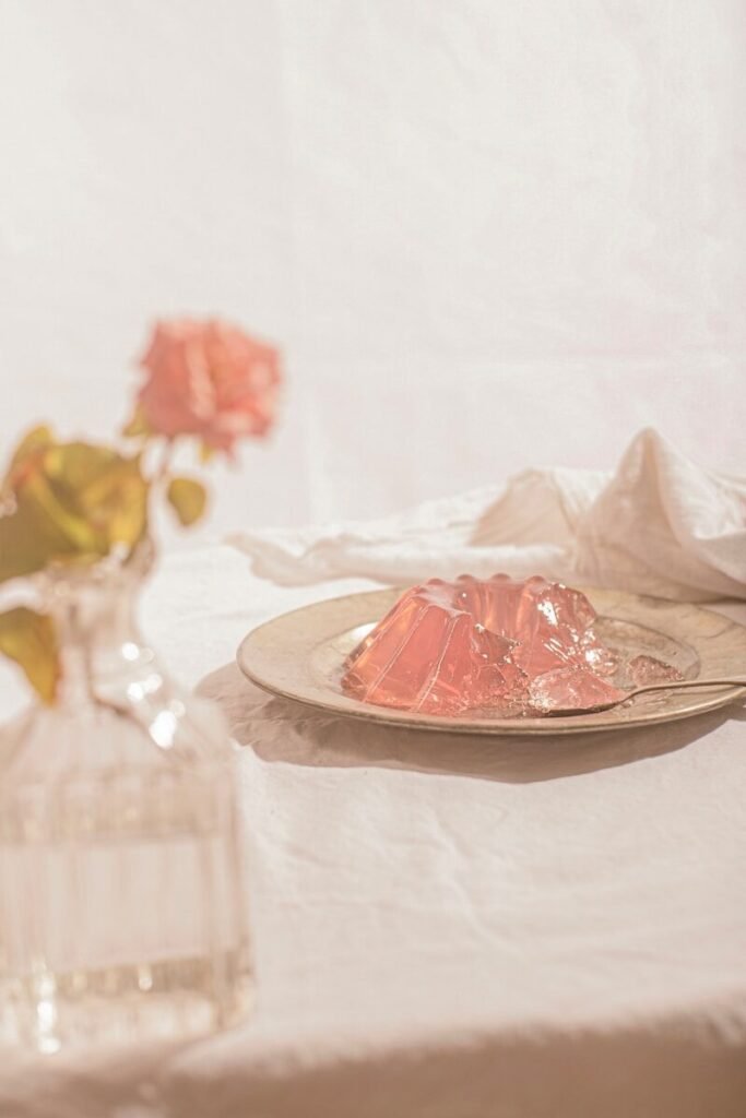 A pink gelatin dessert on a metal plate with a rose in a vase